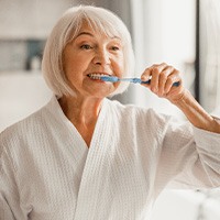 Older woman in a robe and brushing her teeth
