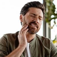 Man holding his cheek and appearing uncomfortable