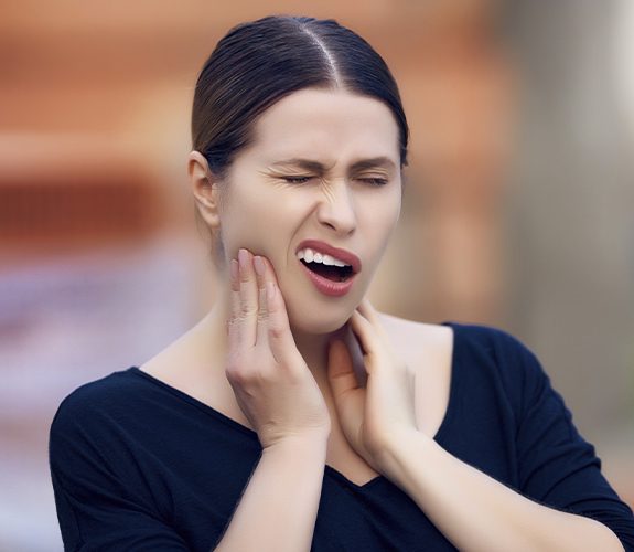 Woman in need of tooth extraction holding jaw in pain