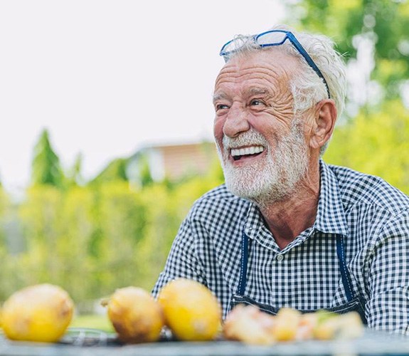 Older man outside at a table showing off implant dentures