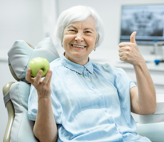 Smiling woman with denture holding an apple and giving a thumbs up