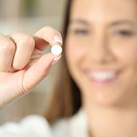Woman holding up a small circular pill