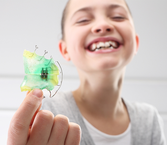Young girl holding up her orthodontic appliance