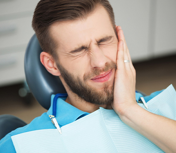 Young man holding cheek in pain at dentist’s office 