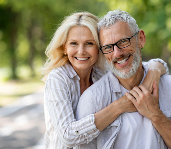 Older man and woman hugging and smiling outside 