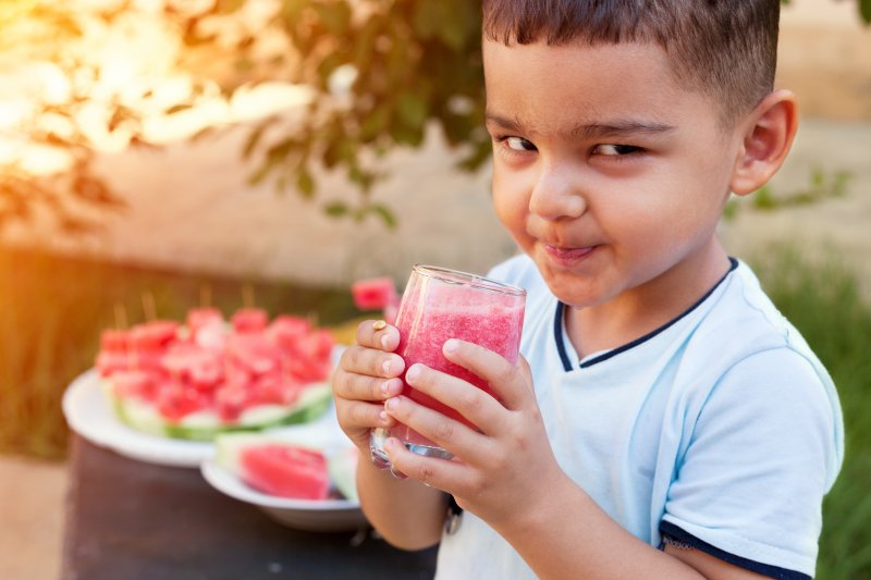 Child drinking watermelon juice in garden with watermelon nearby