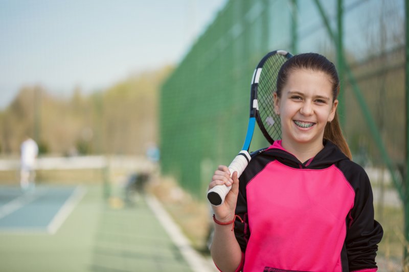 Girl holding tennis racket smiling with braces