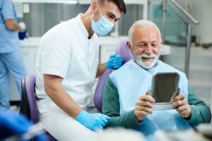An older man smiling in the mirror with new dental implants